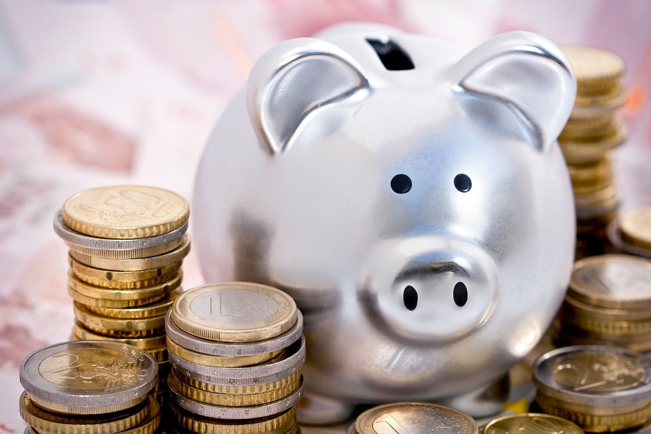 Une tirelire argentée entourée de piles de pièces en euros
